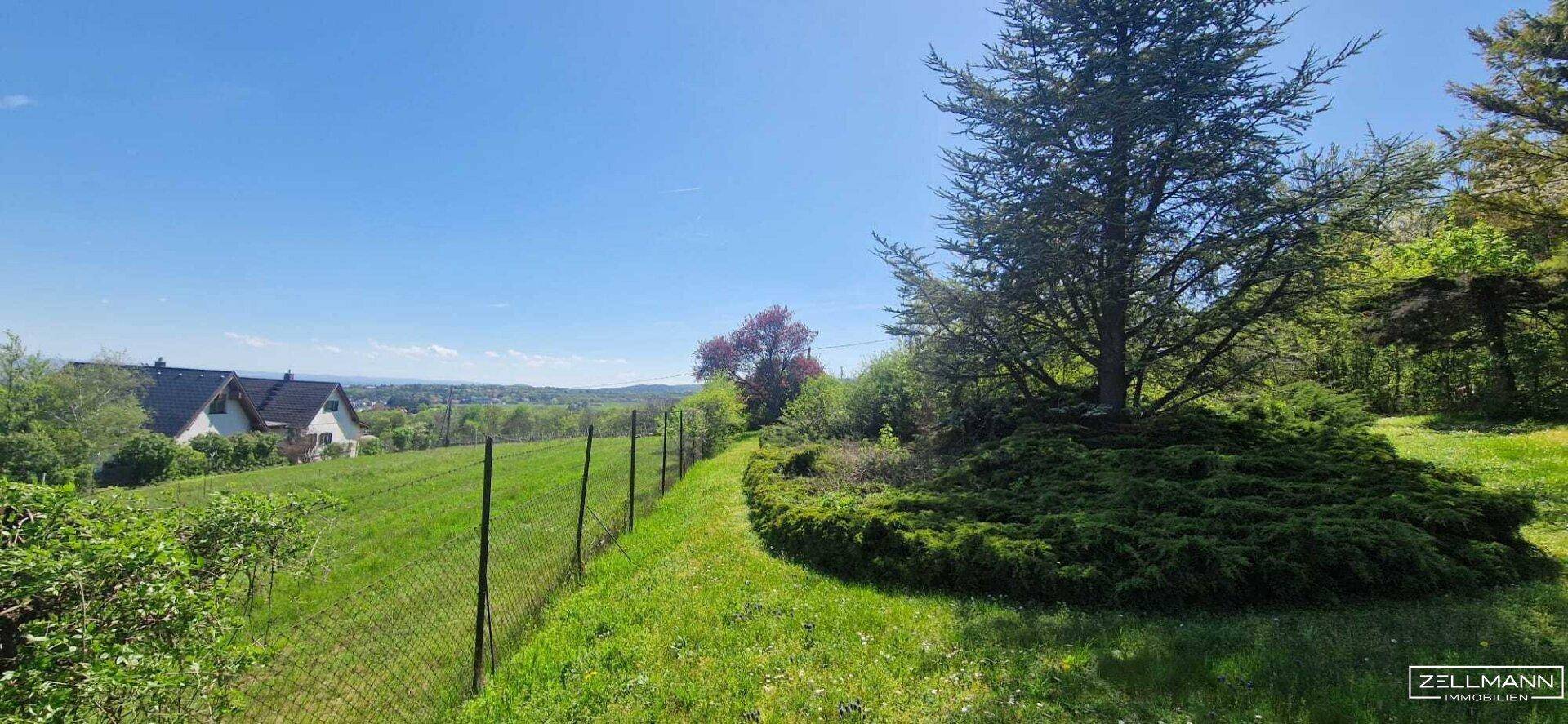 Grünes Grundstück mit Zaunbegrenzung, das einen weiten Blick auf die umliegende Landschaft und Häuser bietet.