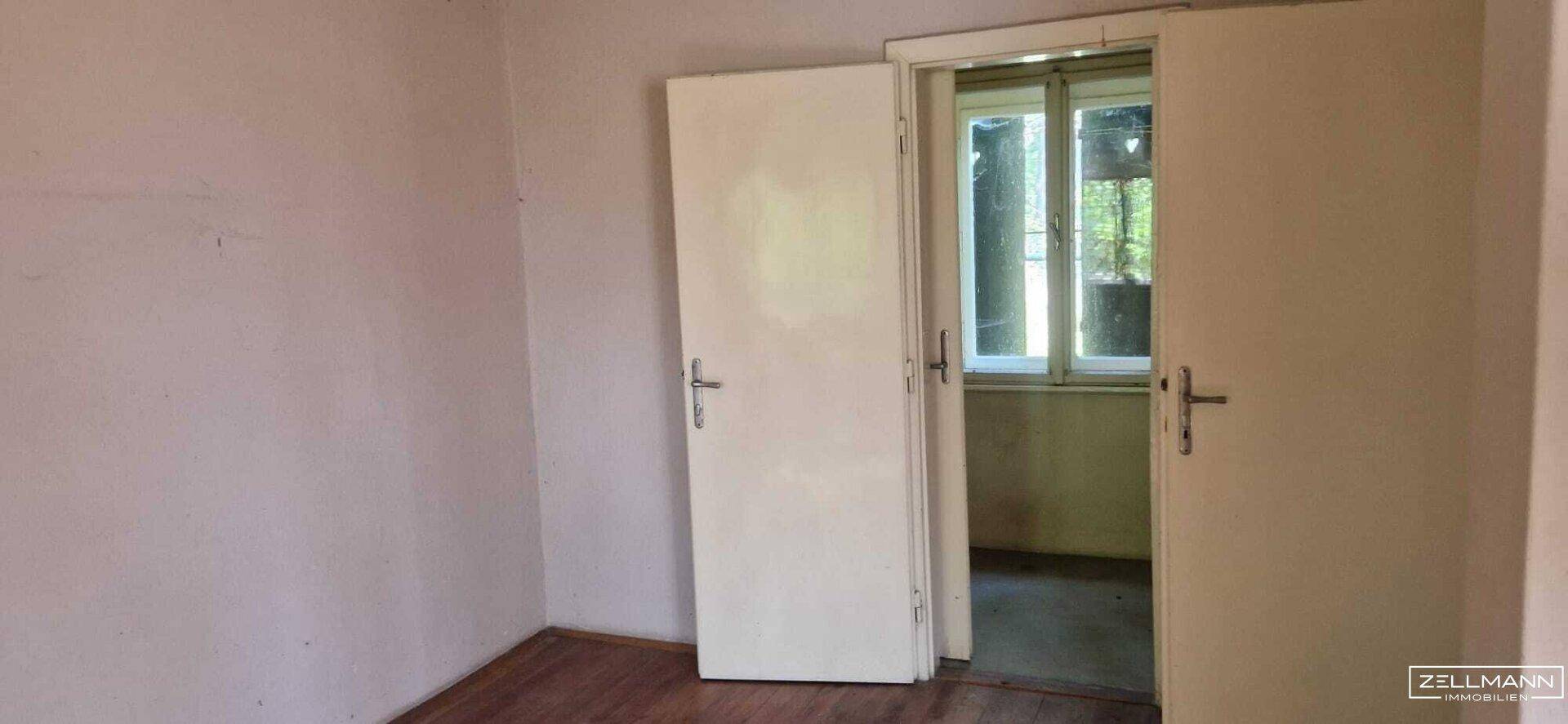 Offener Durchgang zu einem weiteren Raum mit Fenster, die Wände sind in einem hellen Farbton gehalten.