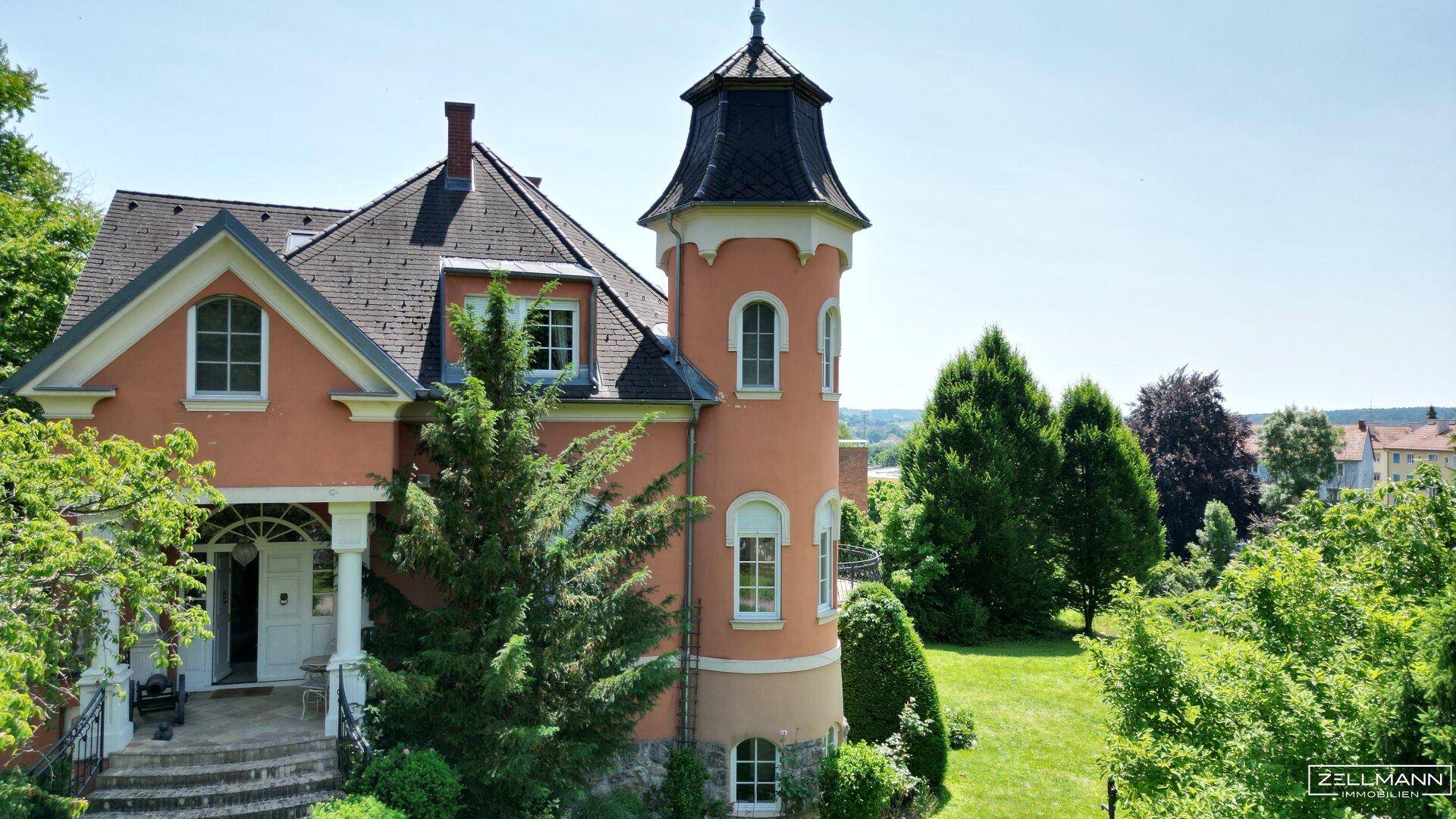 Detailansicht des Haupteingangs und des markanten Turms der Villa, umgeben von üppigem Grün.