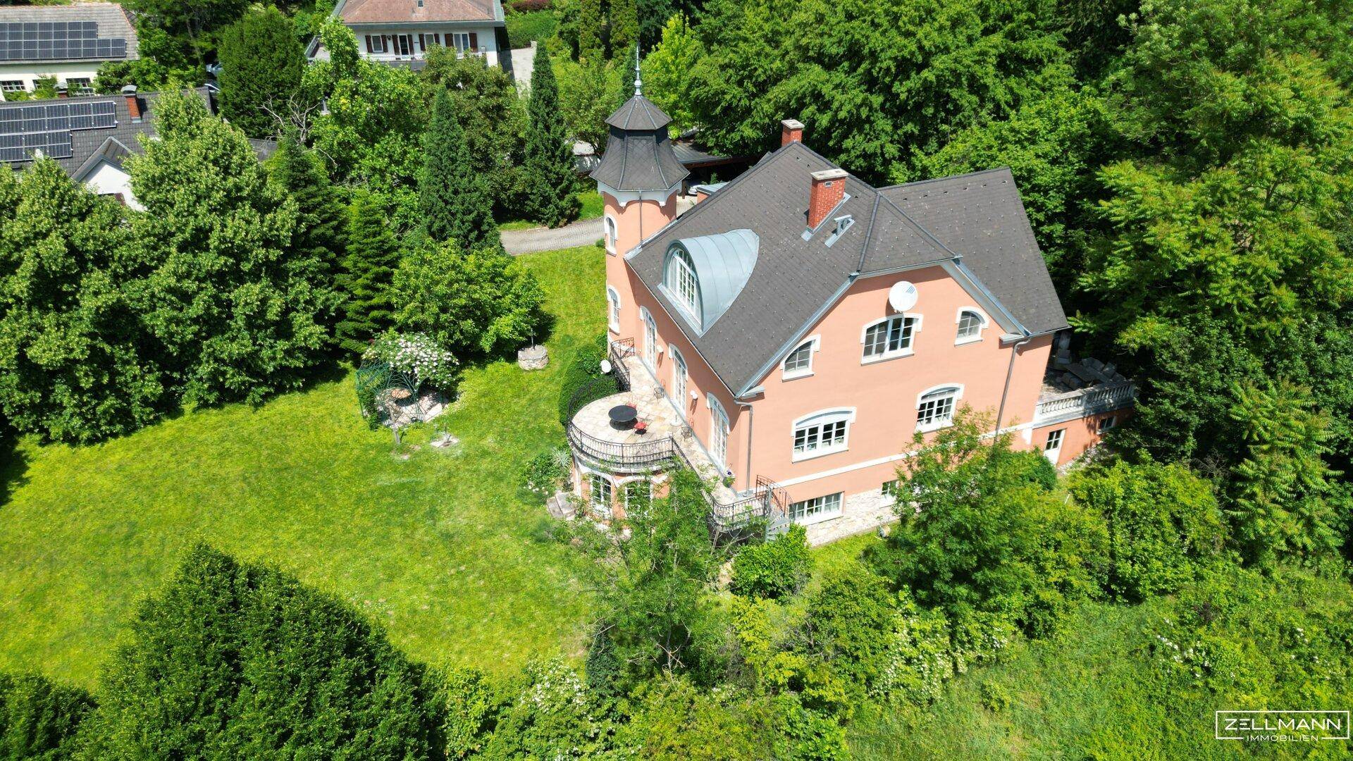 Luftaufnahme der historischen Villa, eingebettet in eine grüne Landschaft mit weiteren Häusern in der Ferne.