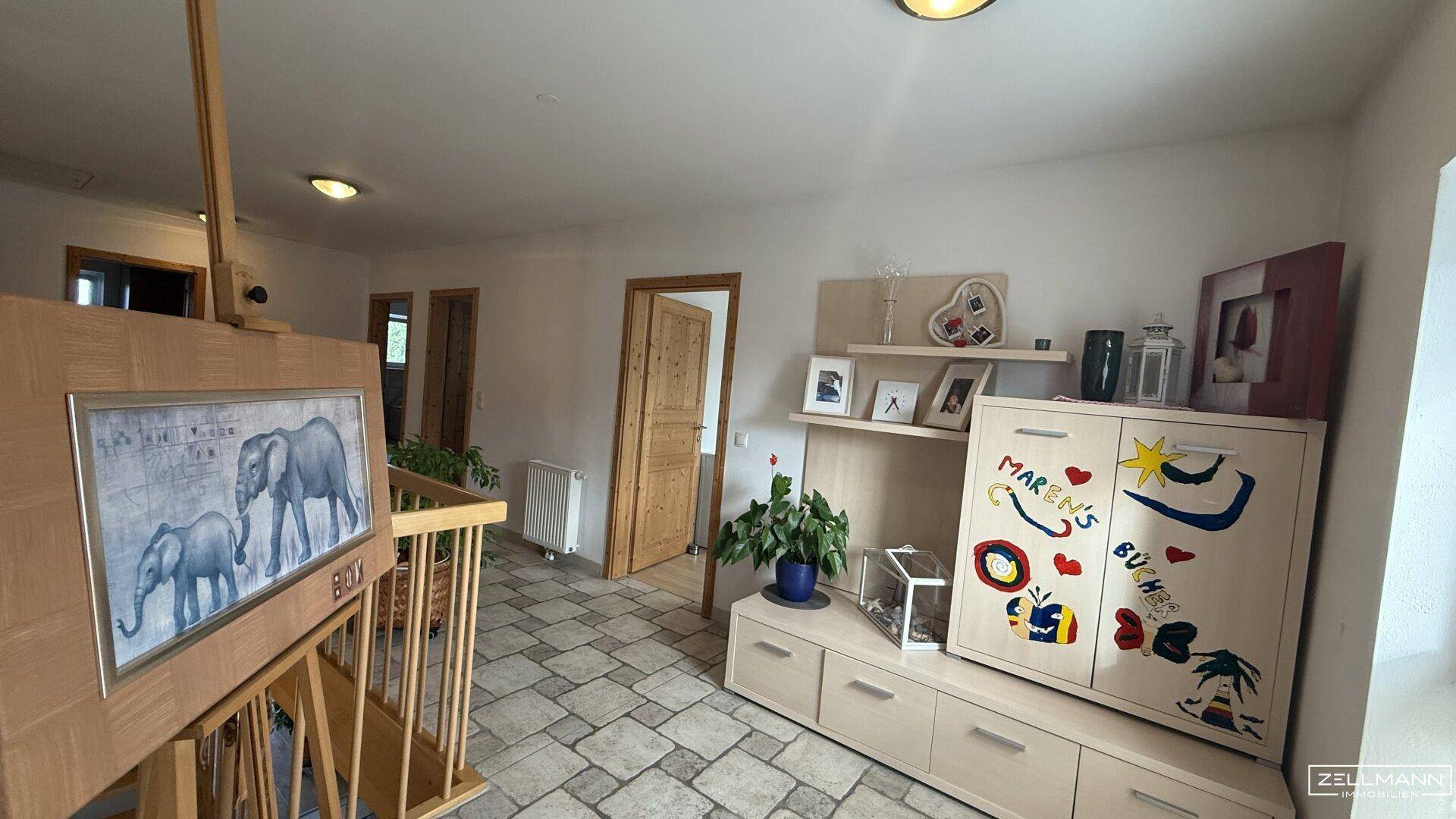 Heller Flur im Obergeschoss mit gefliestem Boden, Holzgeländer und kinderfreundlicher Dekoration.