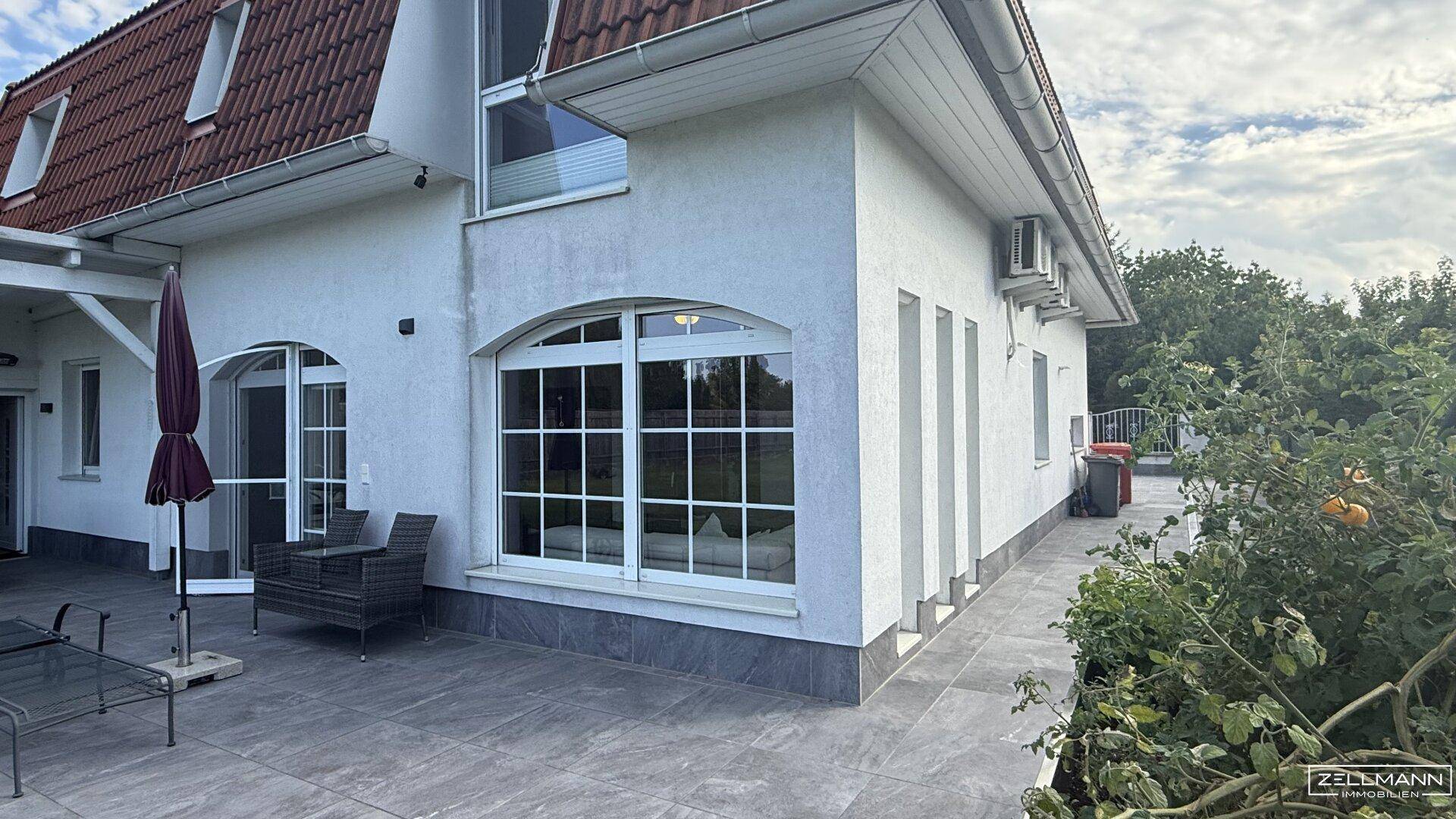 Außenansicht des Hauses mit weißer Fassade, rotem Ziegeldach und einer möblierten Terrasse.
