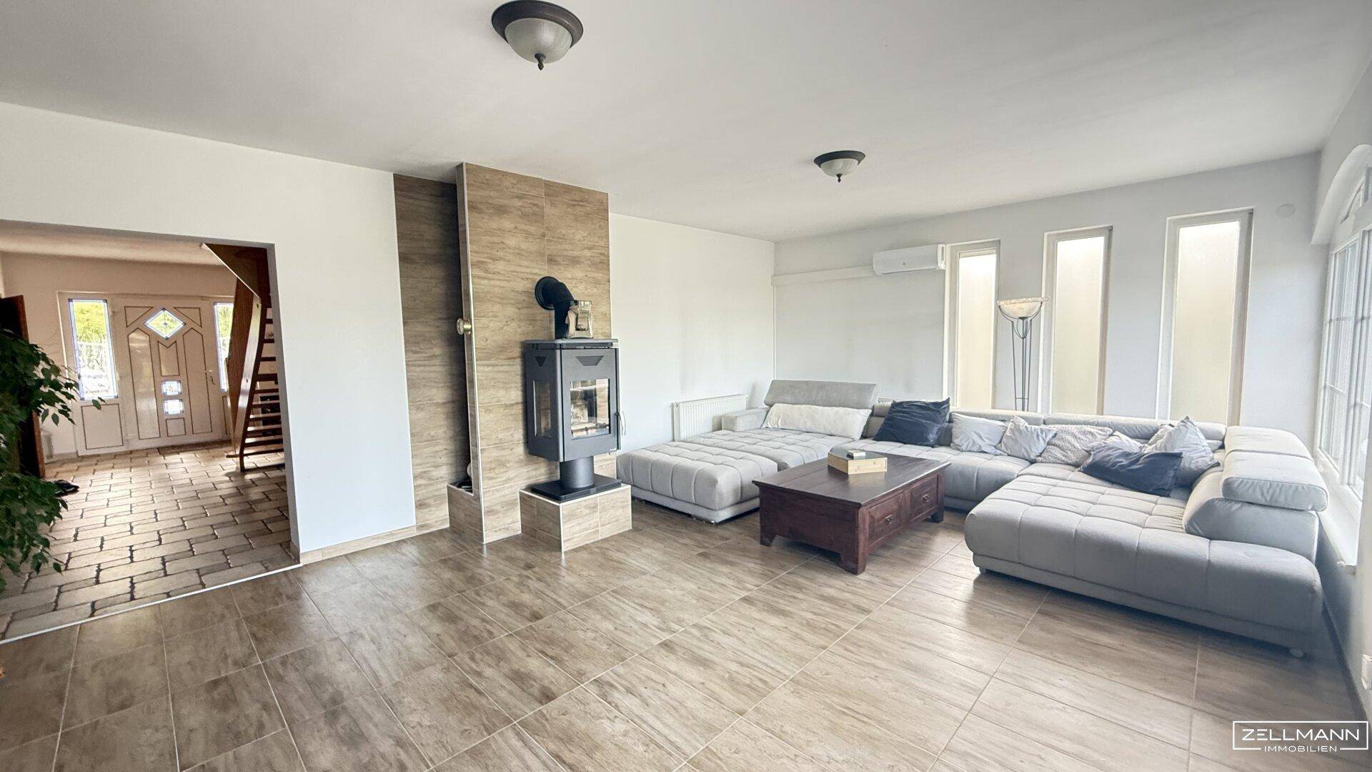 Geräumiges Wohnzimmer mit großem Ecksofa, modernem Holzofen und hellen Fliesenböden.