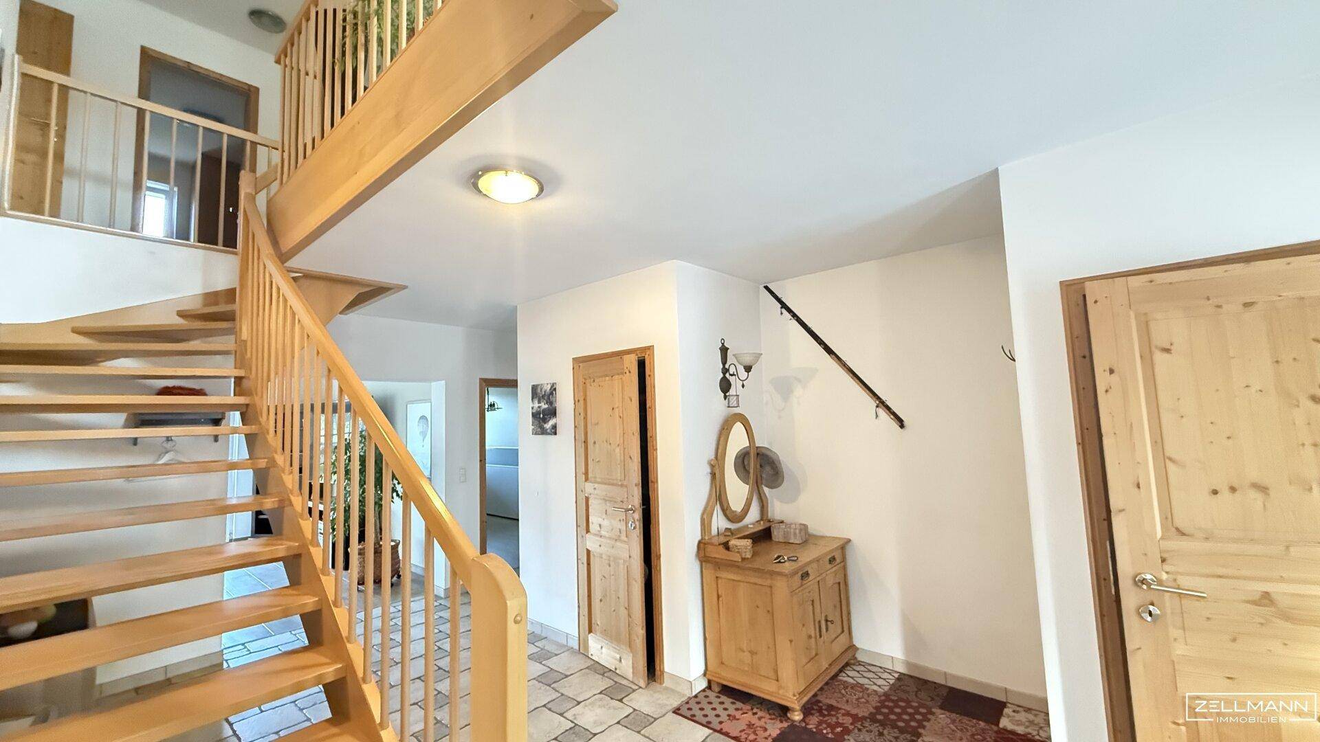 Heller Eingangsbereich mit einer eleganten Holztreppe, gefliestem Boden und rustikalen Holztüren.