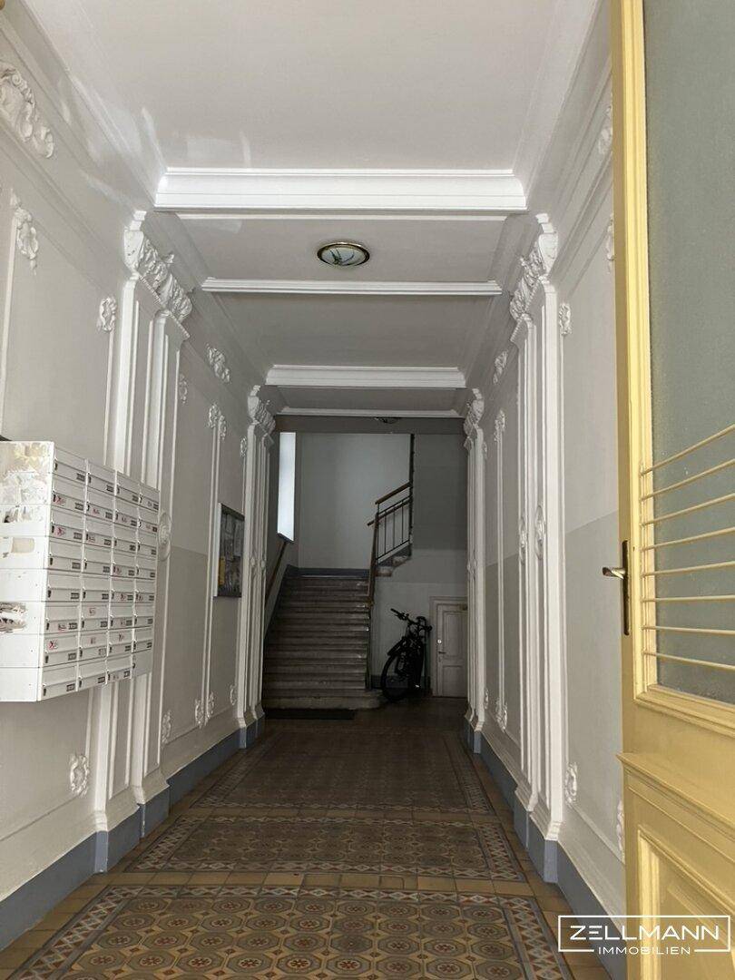 Historischer Eingangsbereich mit Stuckverzierungen, Briefkästen und einer Treppe im Hintergrund.