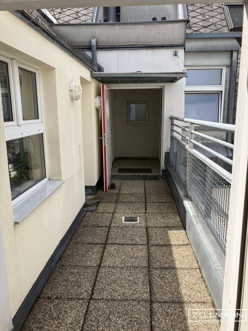 Außenbereich mit gefliestem Boden, Metallgeländer und Zugang zur Wohnung.