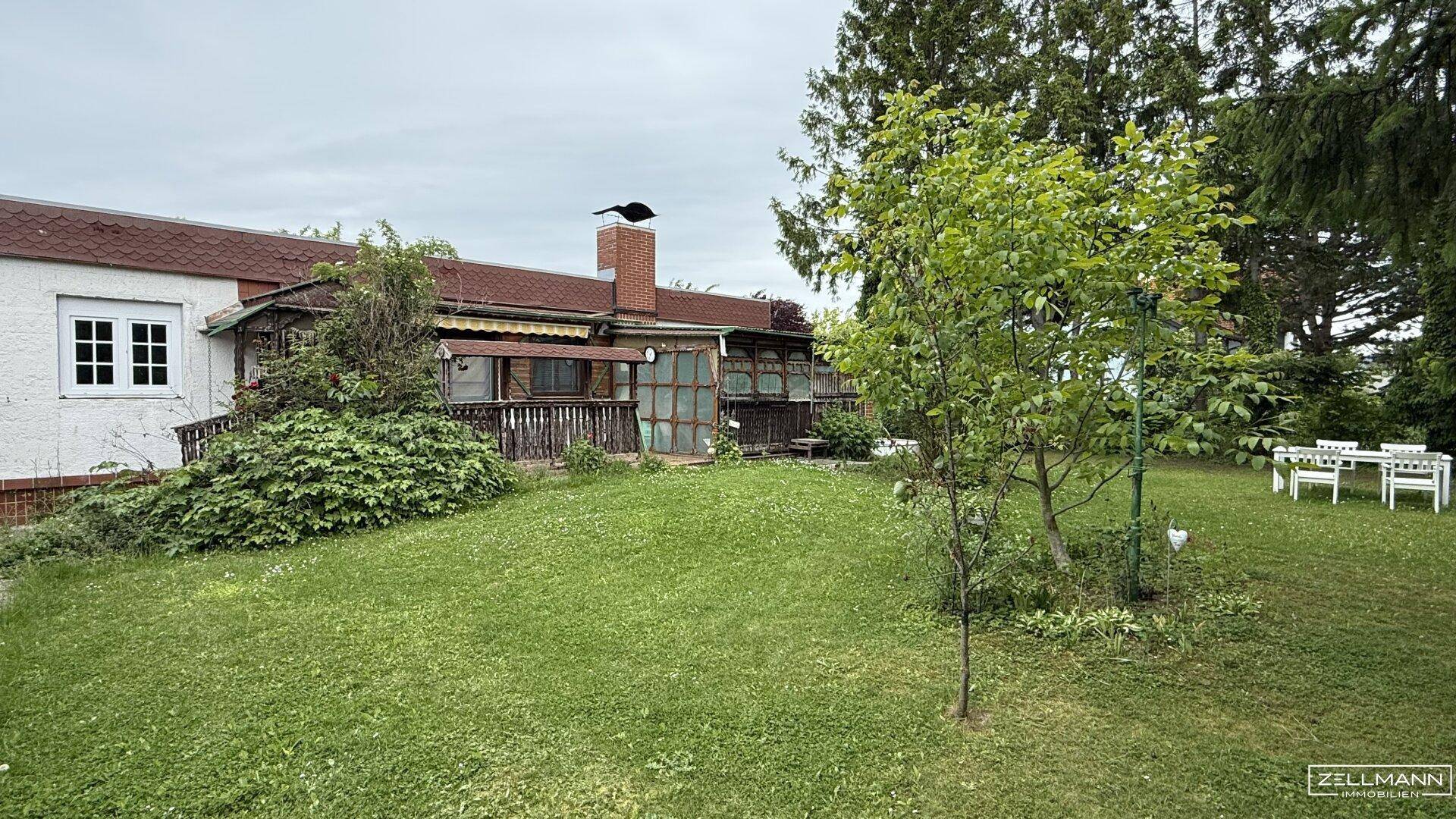 Ruhiger Gartenbereich mit Rasen, Bäumen und einer möblierten Terrasse am Haus.