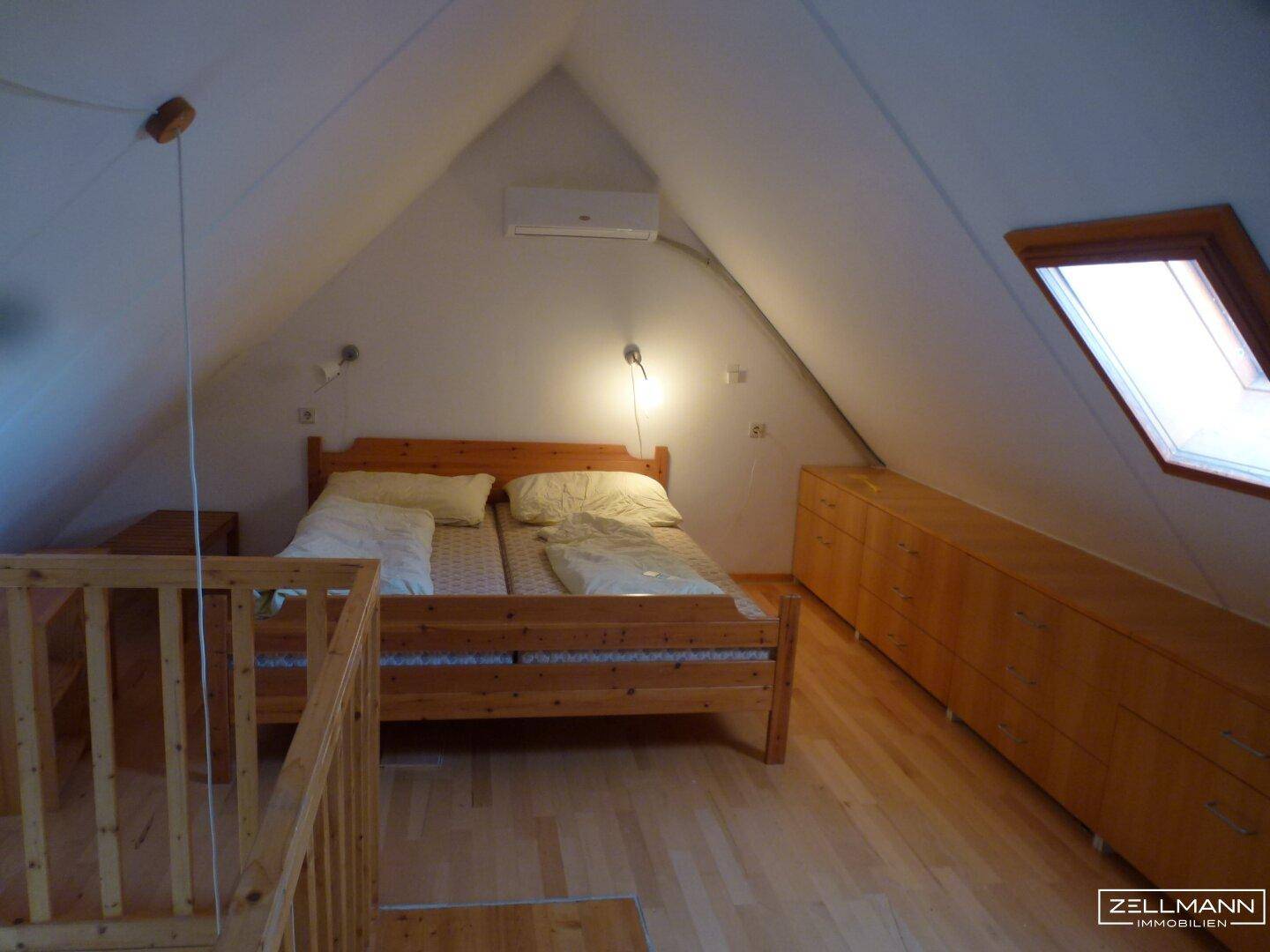 Gemütliches Schlafzimmer im Dachgeschoss mit Holzbett, Dachschräge und Klimaanlage.