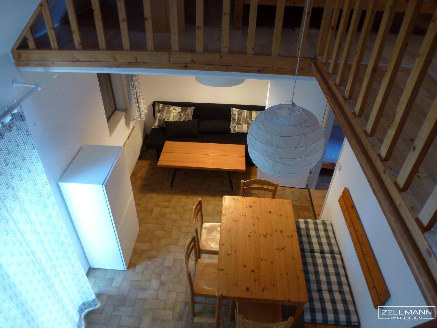 Blick von der Galerie auf den offenen Wohn- und Essbereich mit Holztisch und Sofa.