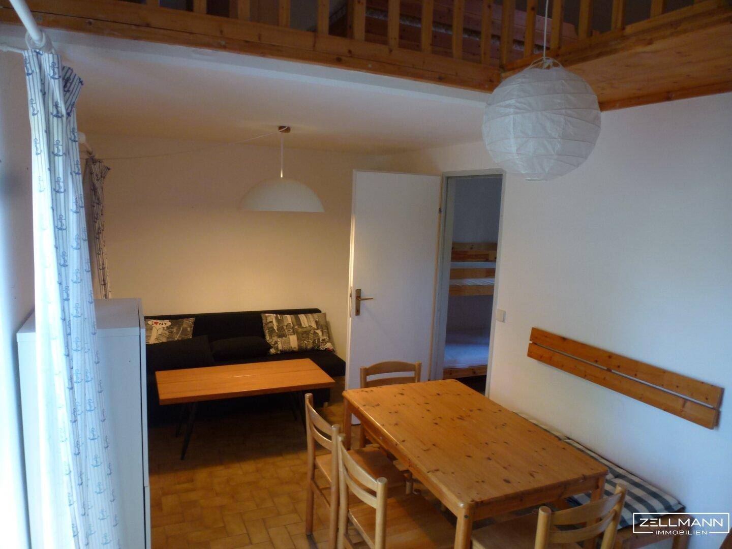 Heller Wohn- und Essbereich mit Esstisch, Sofa und Zugang zu einem weiteren Schlafzimmer.