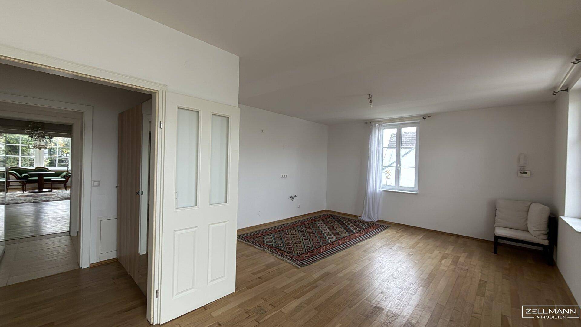 Geräumiges Wohnzimmer mit Holzboden, Teppich und Blick in einen weiteren Raum.