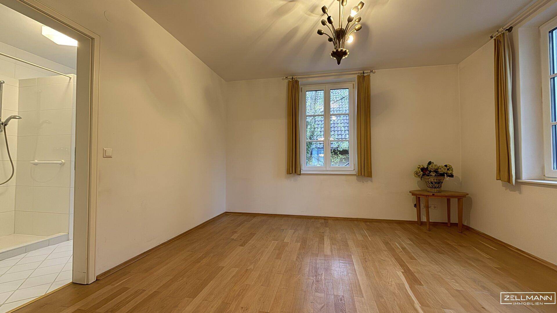 Helles Schlafzimmer mit Holzboden und angrenzendem Badezimmer mit Dusche.