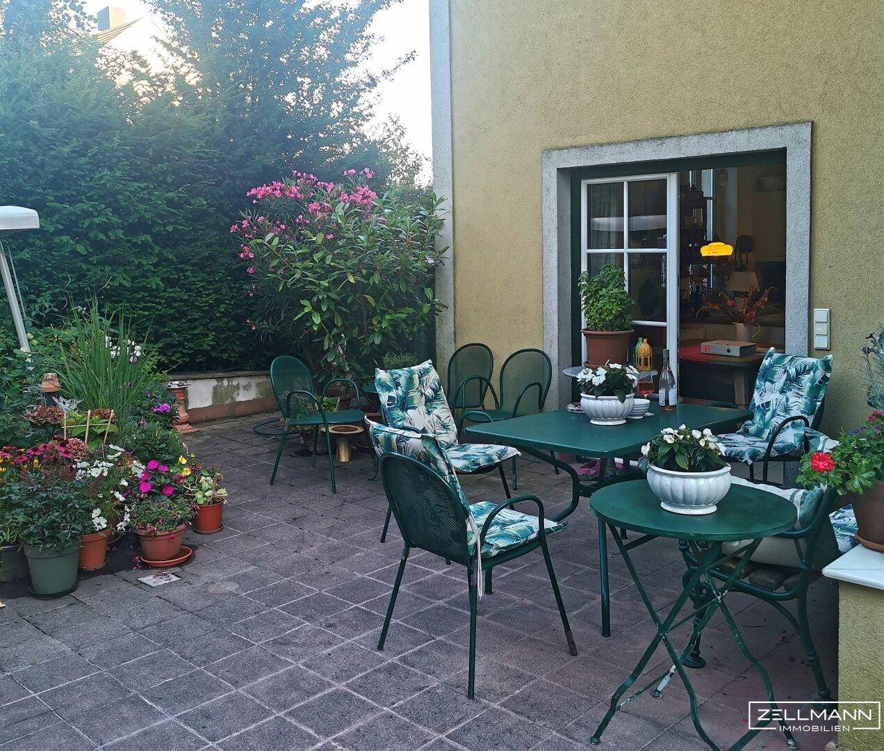 Gemütliche Terrasse mit Gartenmöbeln und üppiger Bepflanzung neben dem Haus.