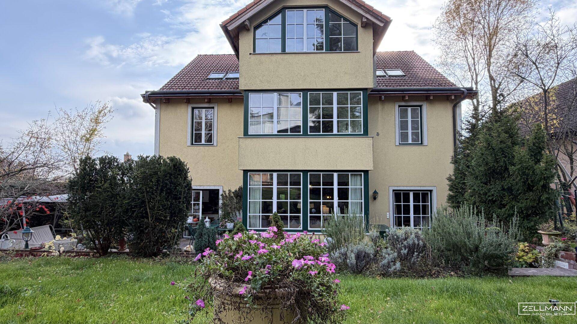 Rückansicht des Hauses mit großem Garten, vielen Fenstern und einer Terrasse im Erdgeschoss.