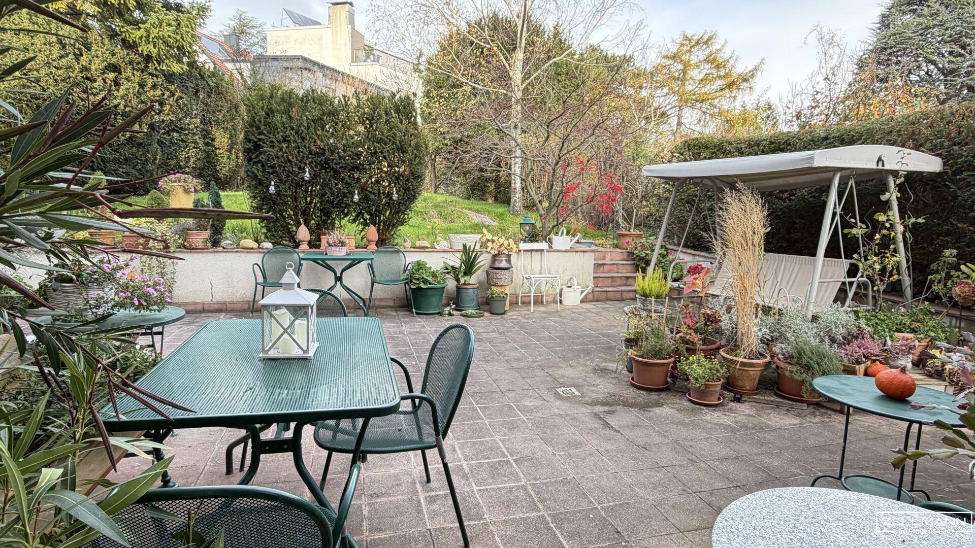 Weitläufige gepflasterte Terrasse mit verschiedenen Sitzbereichen und üppiger Bepflanzung.