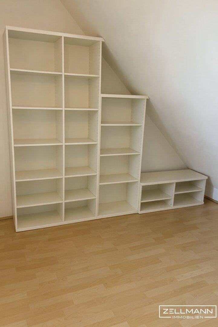 Helles Zimmer mit Laminatboden und weißen Regalsystemen unter der Dachschräge.