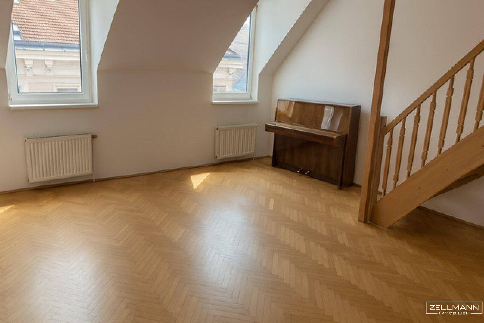 Helles Dachgeschosszimmer mit Fischgrätparkett, Holztreppe und einem Klavier.