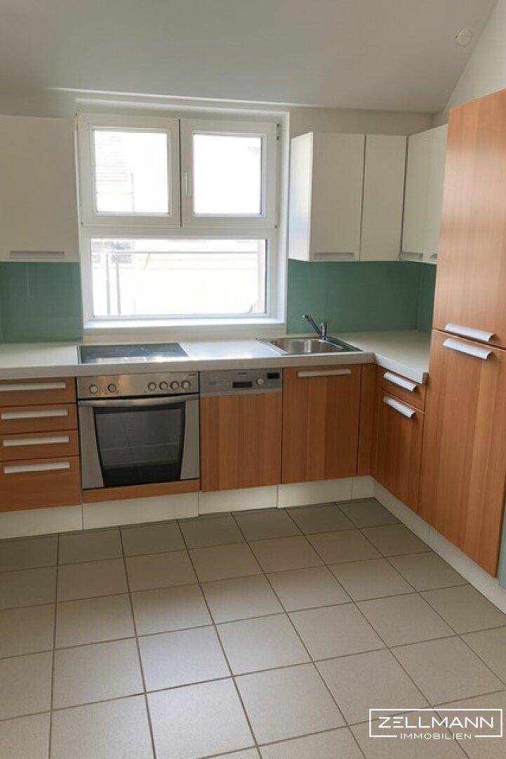 Funktionale Einbauküche mit hellen Holzfronten, weißen Oberschränken und Fliesenboden.