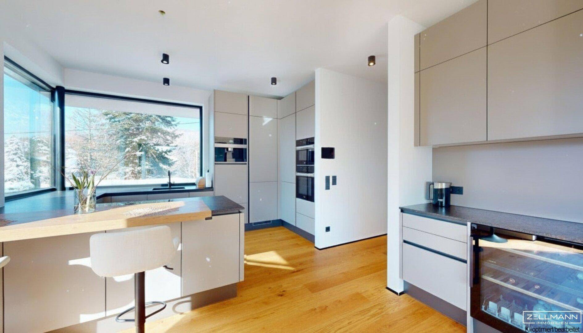 Helle, moderne Küche mit Kücheninsel, großem Fenster und Blick auf die verschneite Landschaft.