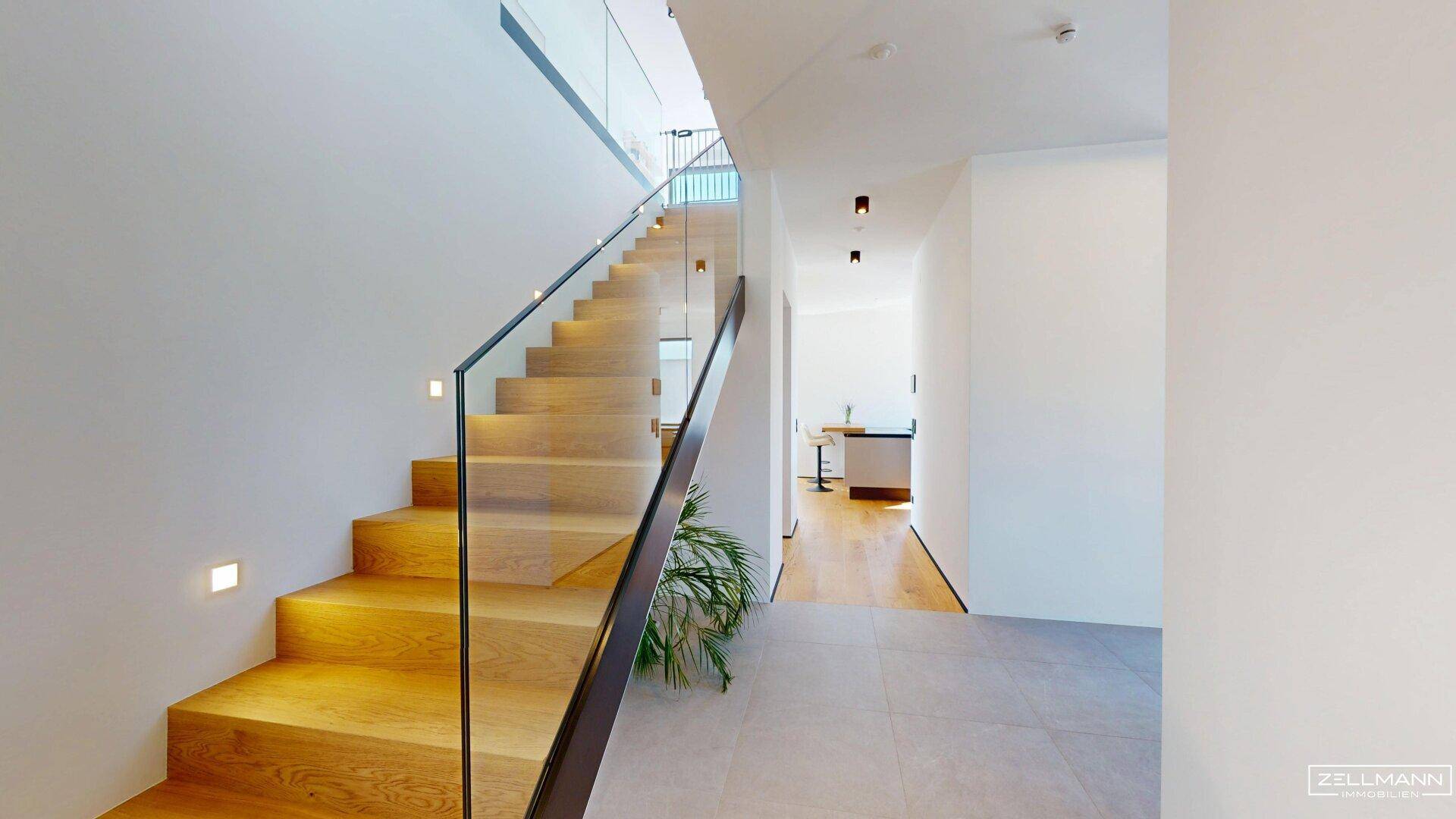 Helle, moderne Treppe mit Holzstufen und elegantem Glasgeländer, die die Etagen verbindet.