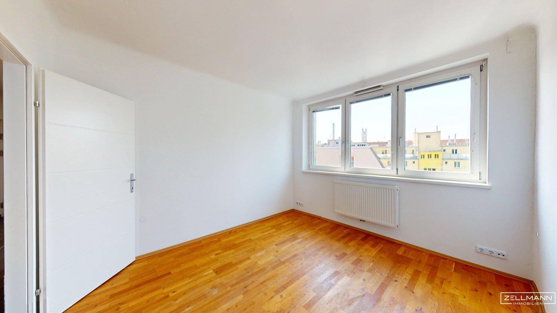 Helles Schlafzimmer mit Holzboden und großen Fenstern, die einen Blick nach draußen ermöglichen.