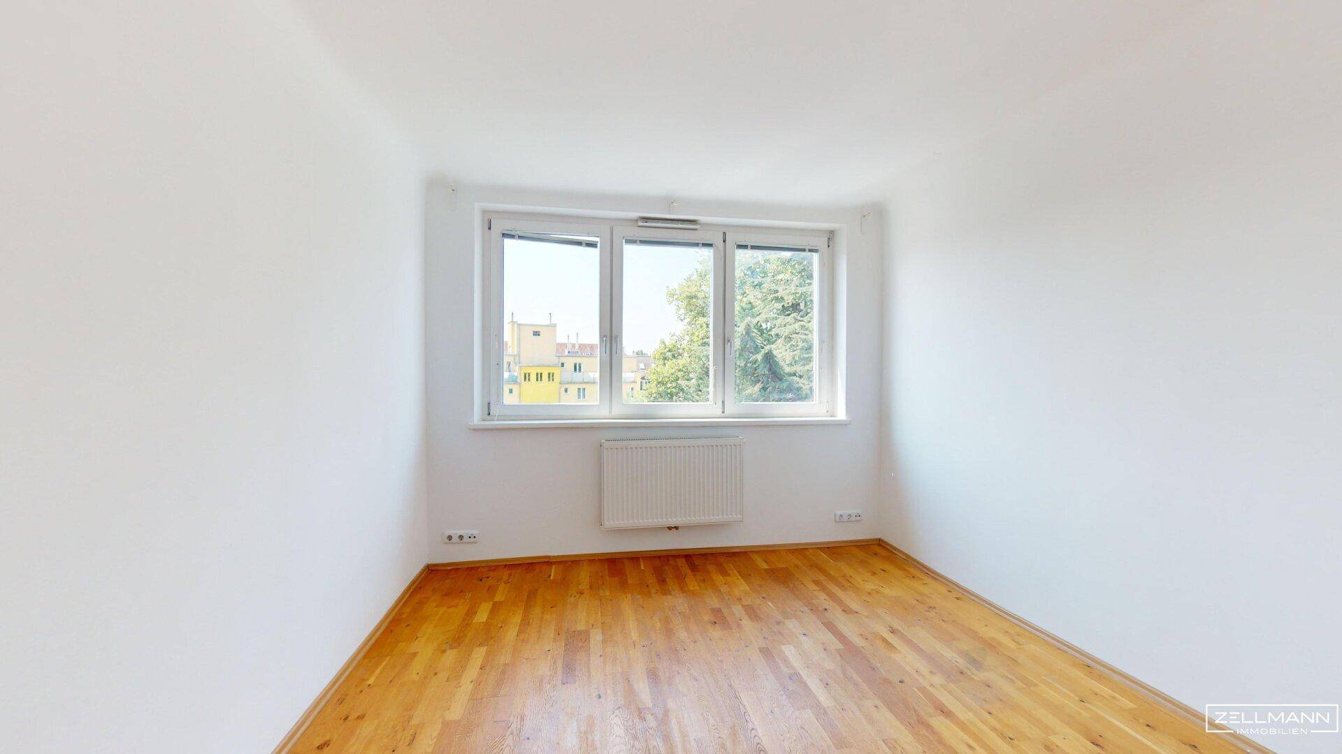 Geräumiges, helles Schlafzimmer mit Holzboden und großen Fenstern, die viel Licht spenden.