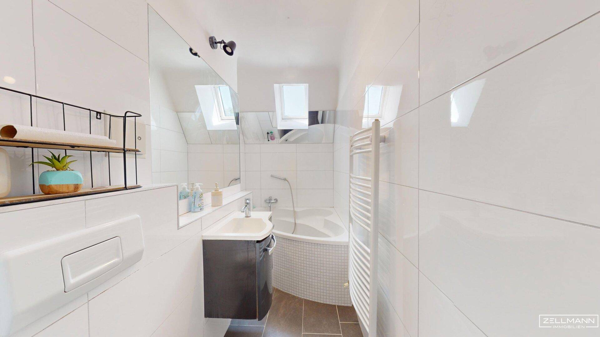 Modernes Badezimmer mit weißen Fliesen, Badewanne, Waschbecken und Dachfenstern für Tageslicht.