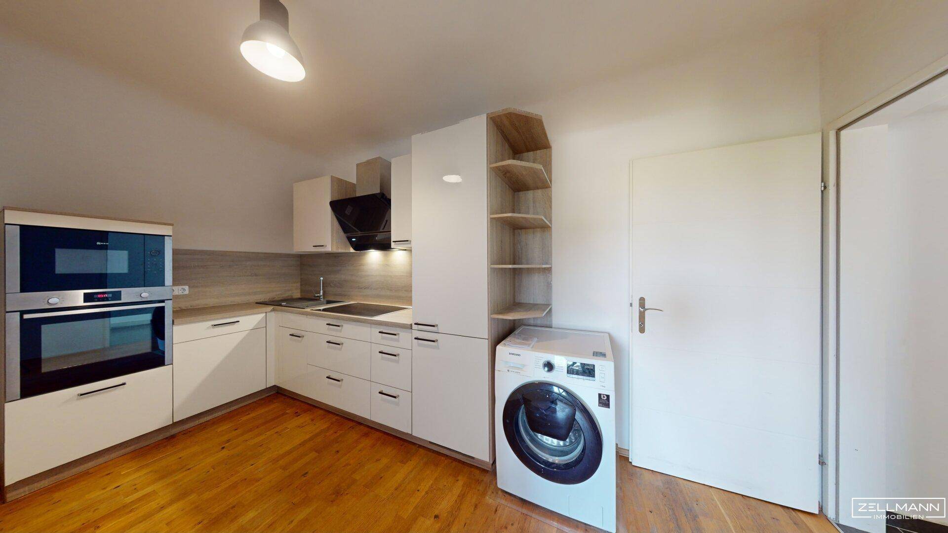 Moderne Einbauküche mit weißen Schränken, integrierten Geräten und einer Waschmaschine.