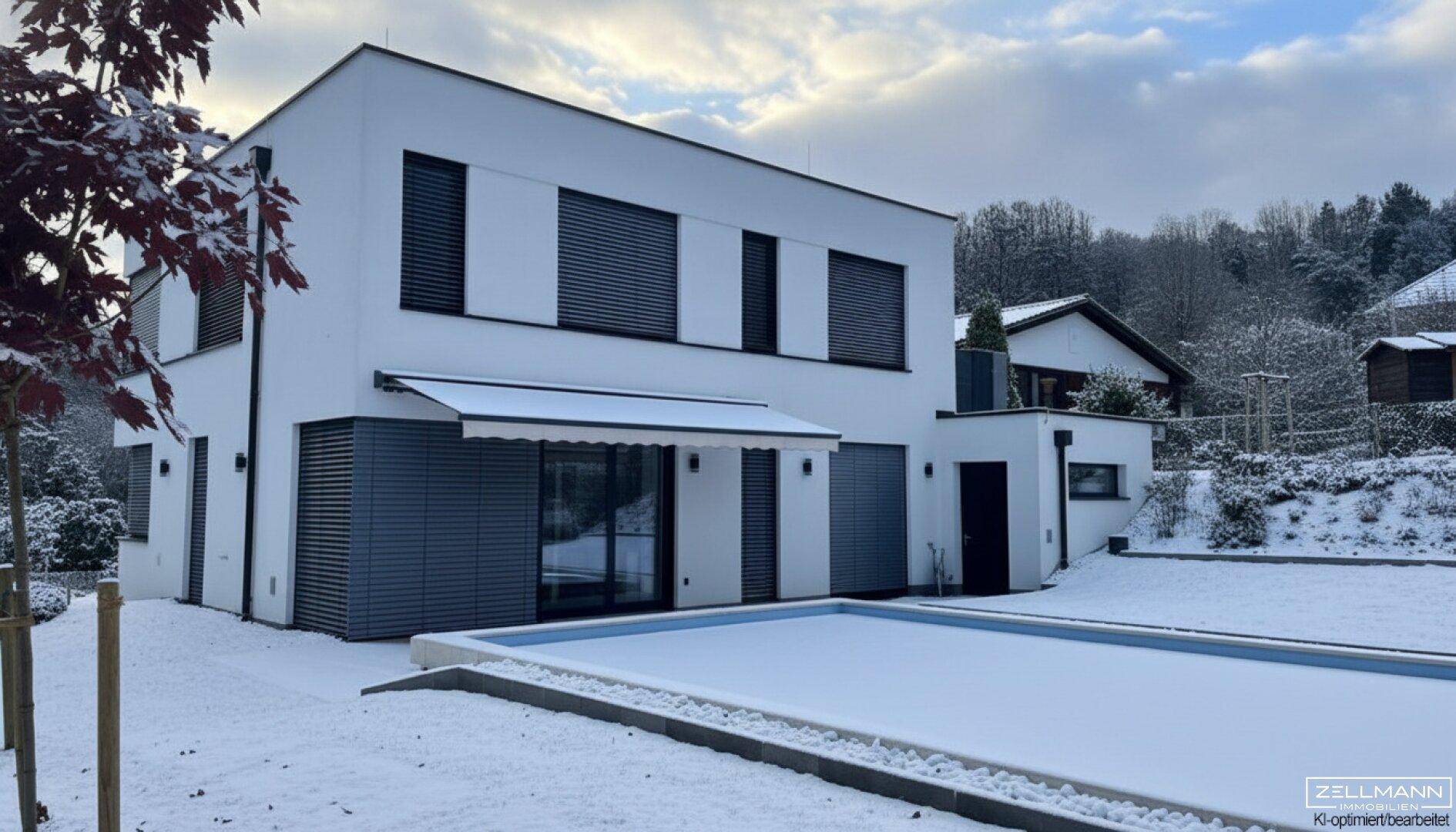 Modernes Einfamilienhaus mit Garten und Pool, umgeben von einer verschneiten Winterlandschaft.