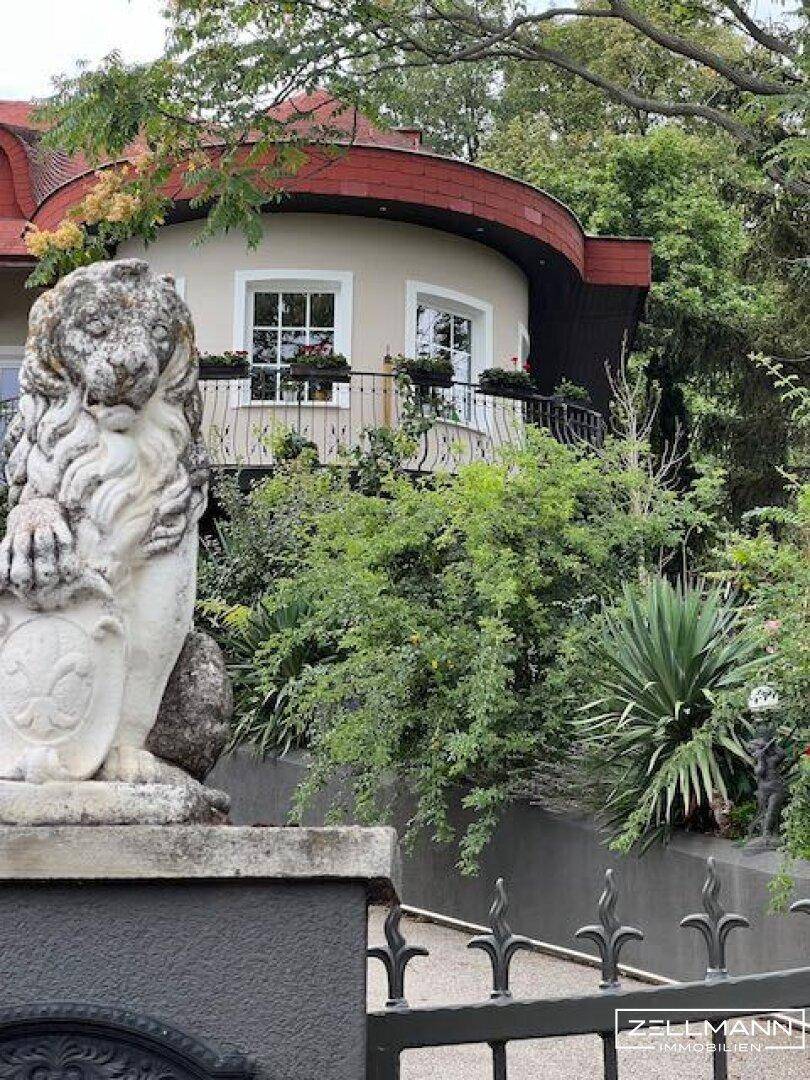 Historische Villa mit dekorativer Löwenstatue am Eingang und üppigem Garten.