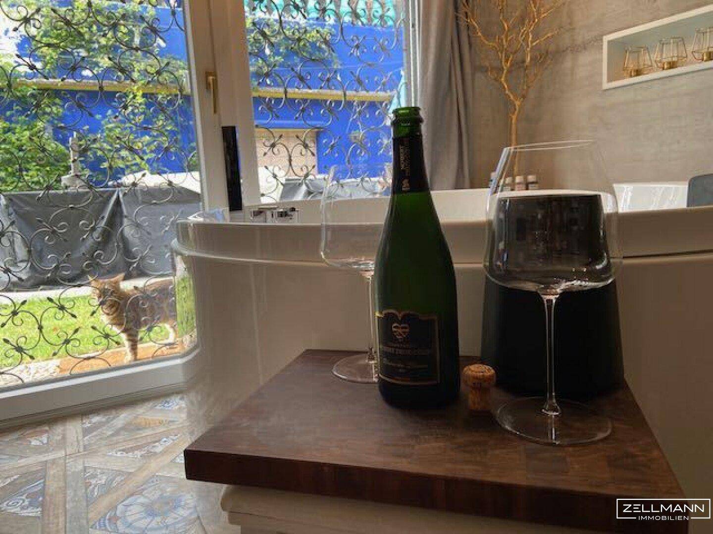 Modernes Badezimmer mit freistehender Badewanne, Blick ins Grüne und Sektflasche.