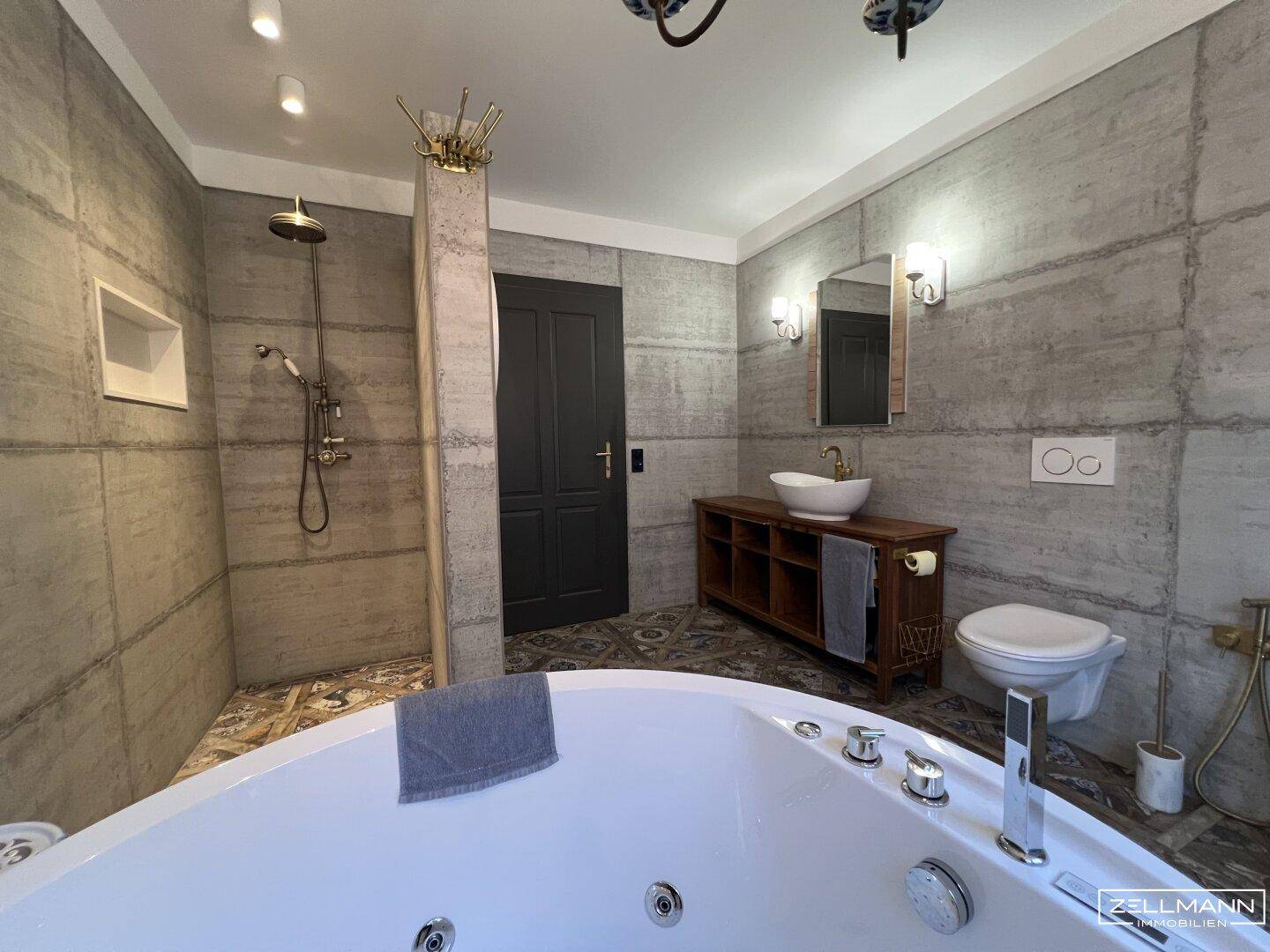 Geräumiges Badezimmer mit begehbarer Dusche, Whirlpool-Badewanne und Betonelementen.