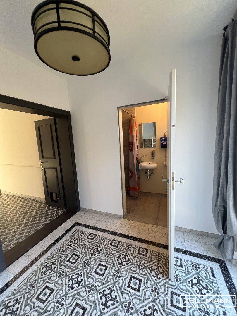 Flur mit gemustertem Fliesenboden und Blick in ein angrenzendes Badezimmer.