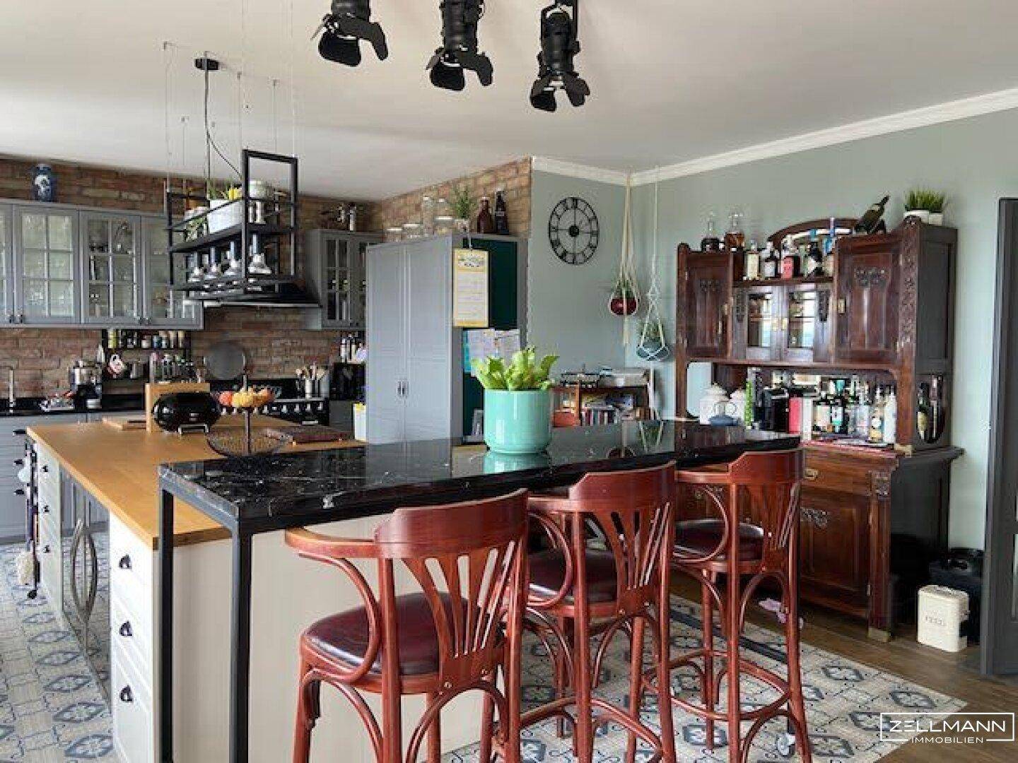 Offene Küche mit Kücheninsel, Barhockern und Backsteinwand im Landhausstil.