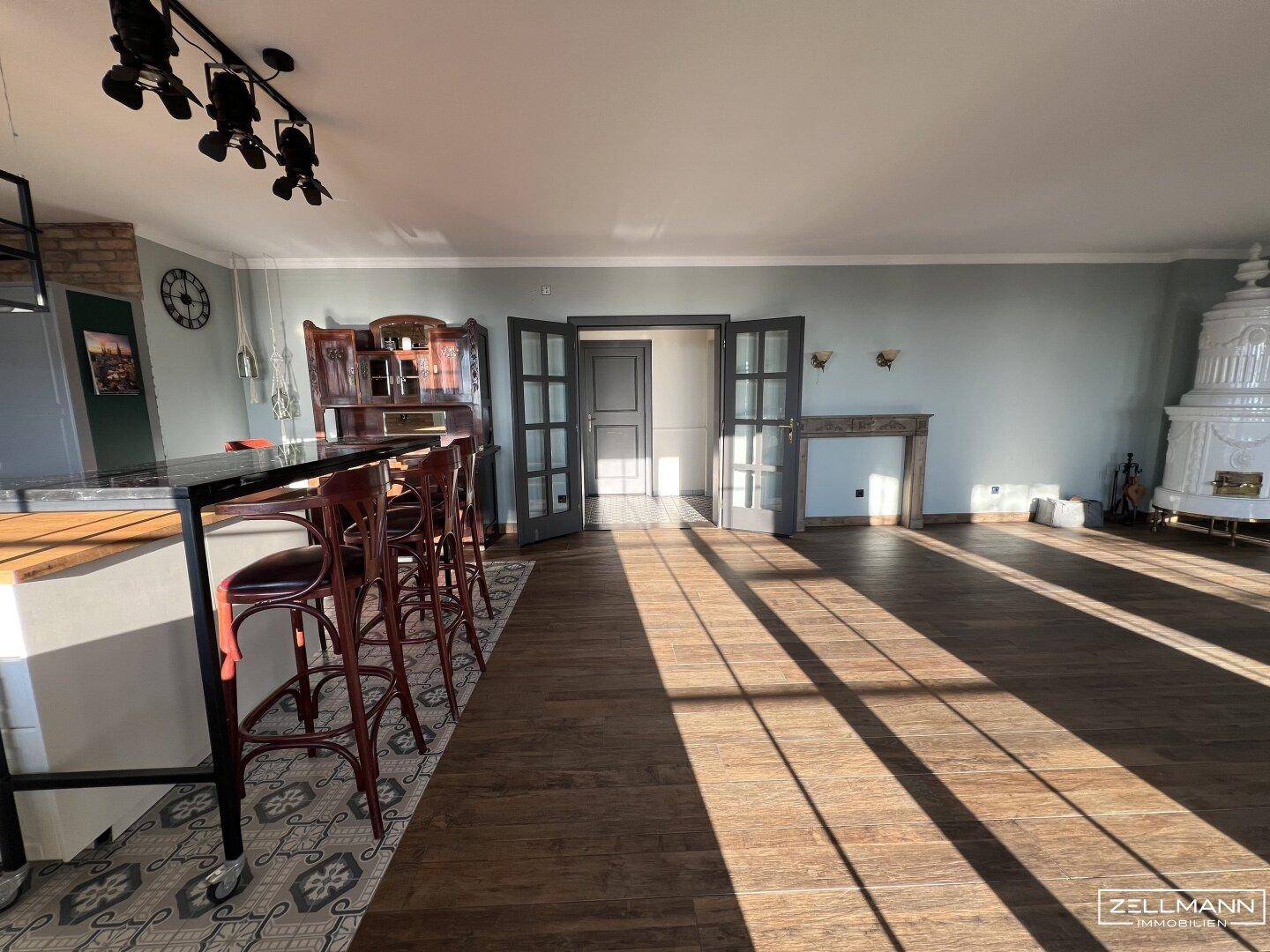 Heller Wohnbereich mit Holzboden, Kachelofen und Blick auf den Garten.