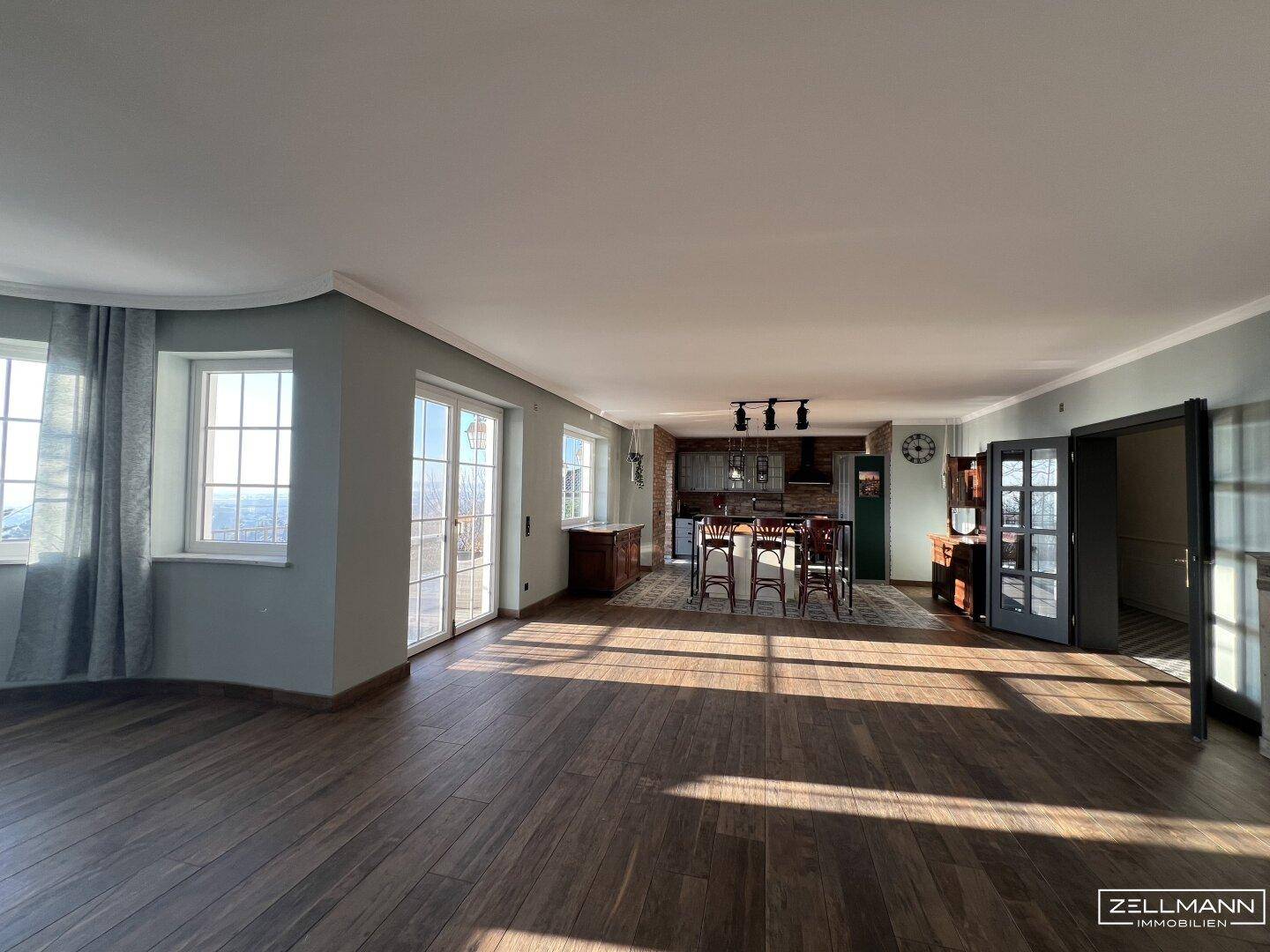 Großzügiger Wohnbereich mit Holzboden, großen Fenstern und viel natürlichem Licht.