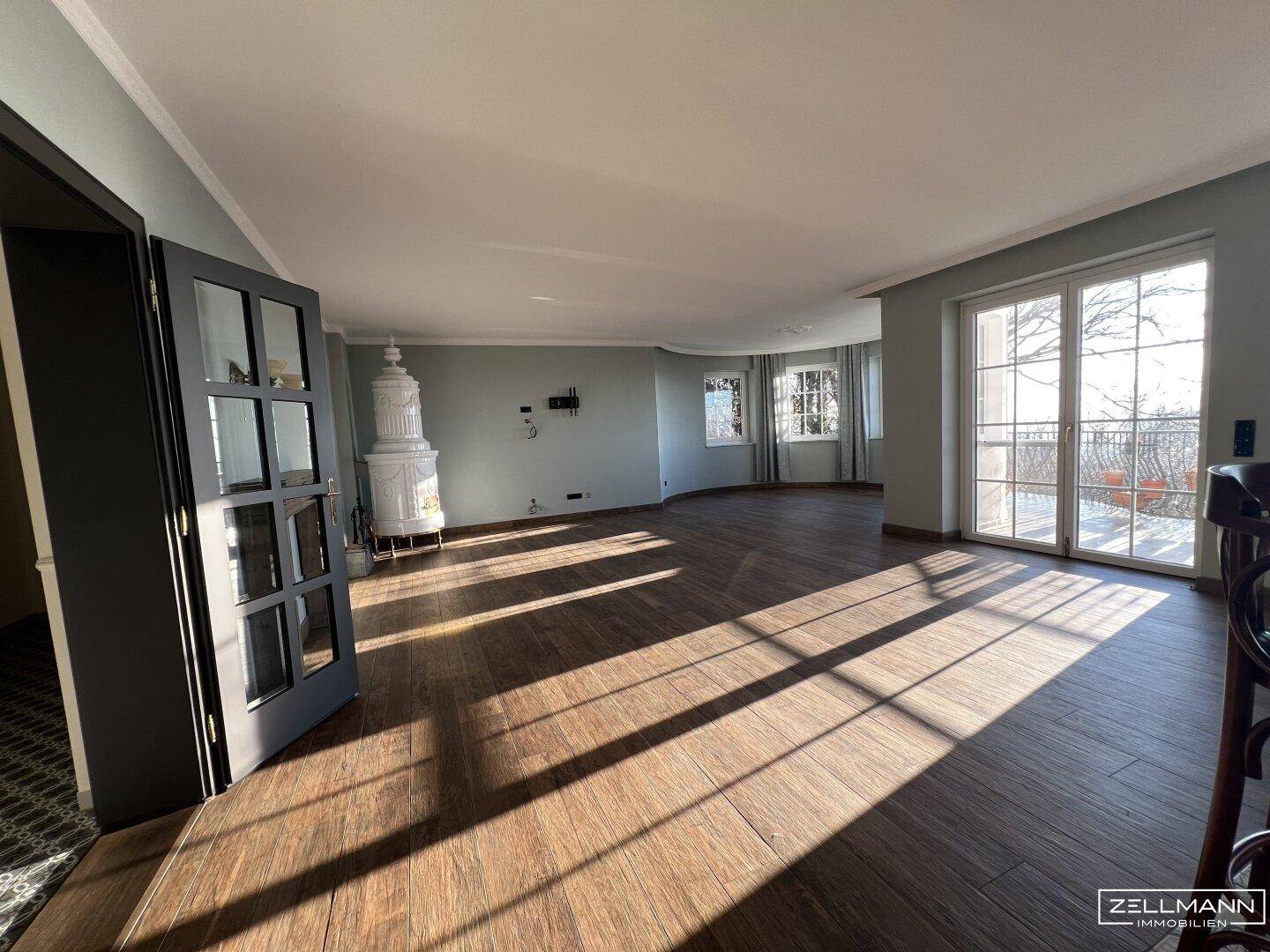 Heller Wohnbereich mit Holzboden, Kachelofen und Zugang zur Terrasse.