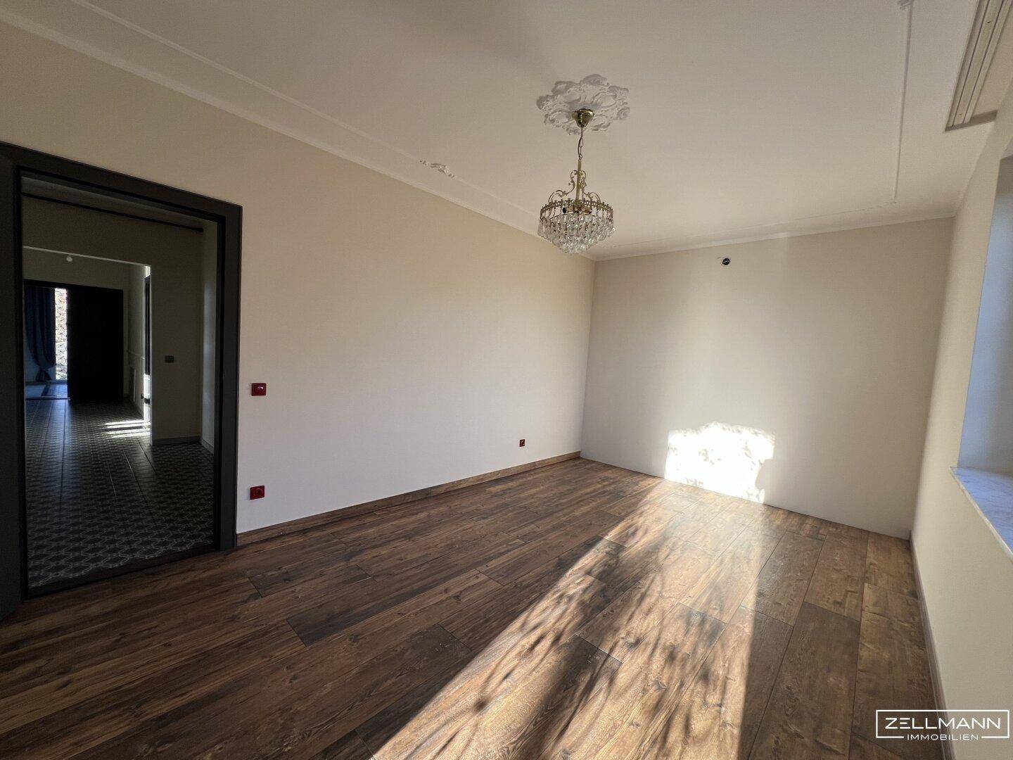 Helles Schlafzimmer mit Holzboden, Stuckdecke und Kronleuchter.