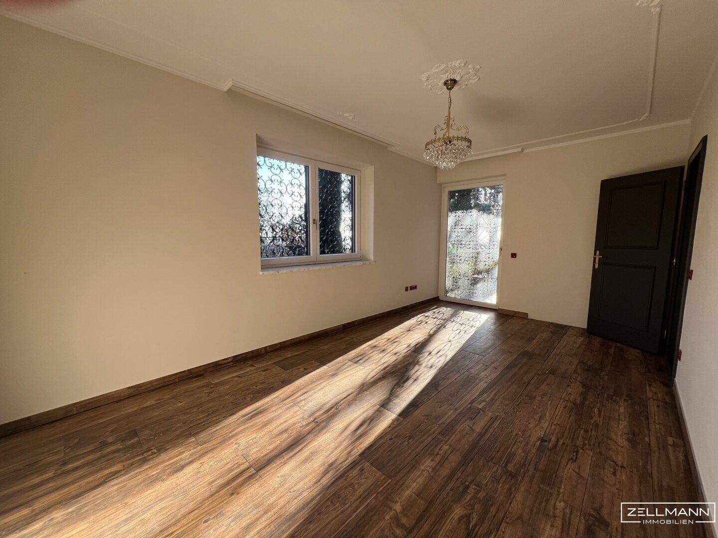 Schlafzimmer mit Holzboden, Fenster und Zugang zu einem Außenbereich.