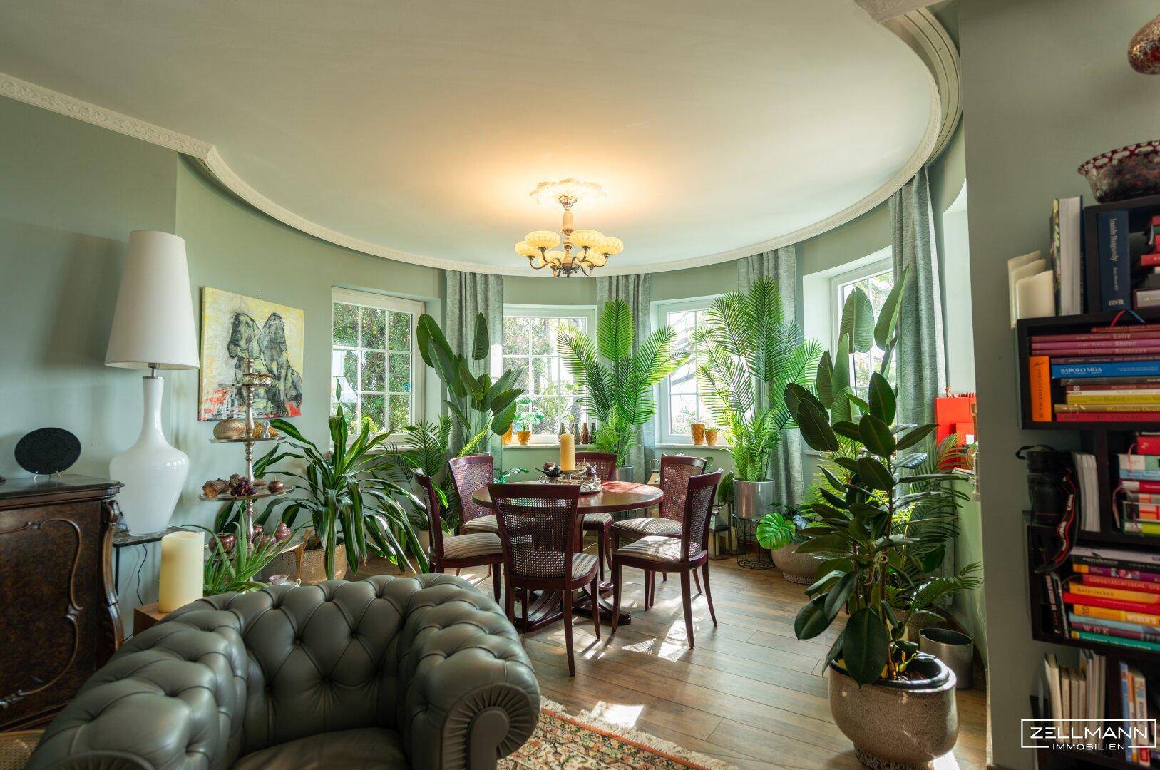 Heller Wohnbereich mit vielen Pflanzen, runden Fenstern und klassischer Einrichtung.
