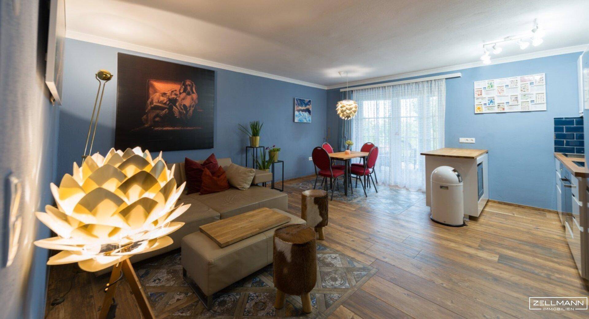 Heller Wohn-Essbereich mit blauen Wänden, Holzboden und Zugang zum Balkon.