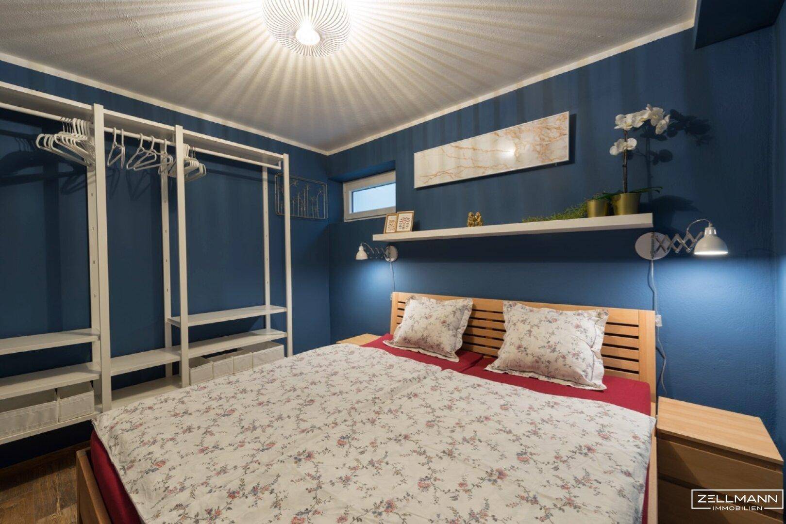 Schlafzimmer mit blauen Wänden, Holzbett und offenem Kleiderschrank.