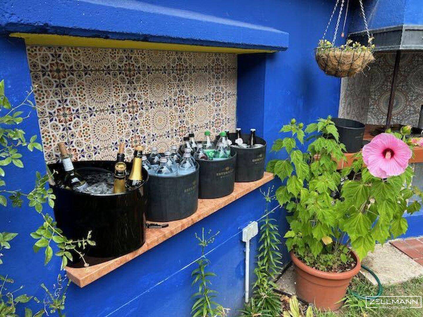 Bunte Außenbar mit marokkanischen Fliesen und Getränkekühlern im Gartenbereich.