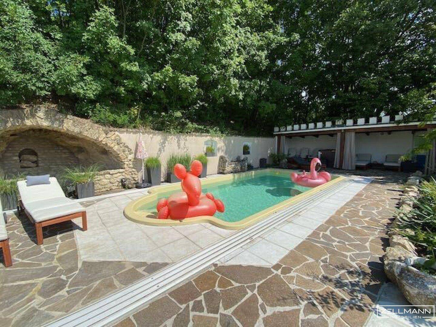 Großer Außenpoolbereich mit Sonnenliegen, Pergola und gepflasterter Terrasse.