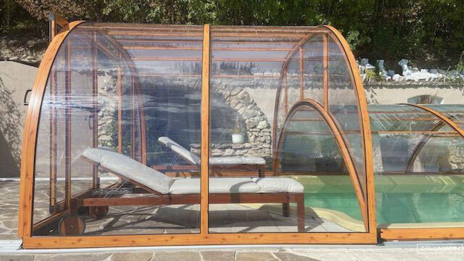 Transparente Poolüberdachung mit Sonnenliege, die Schutz und Komfort bietet.