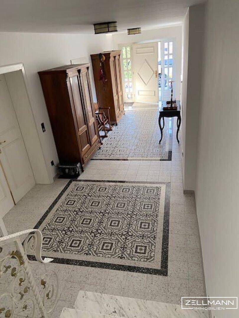 Geräumiger Eingangsbereich mit gemustertem Fliesenboden, Holzschränken und Zugang zur Treppe.