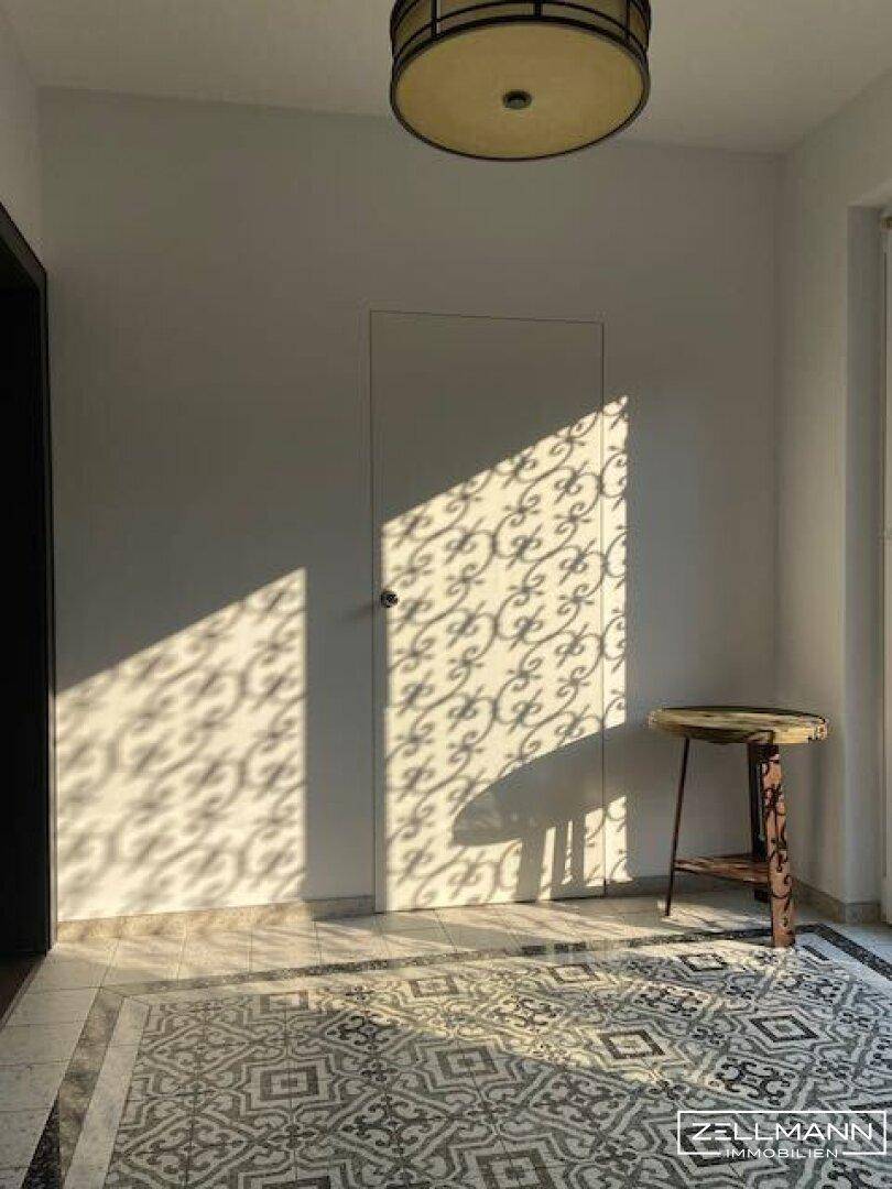 Heller Flur mit gemustertem Fliesenboden und dekorativen Lichteffekten durch Sonneneinstrahlung.