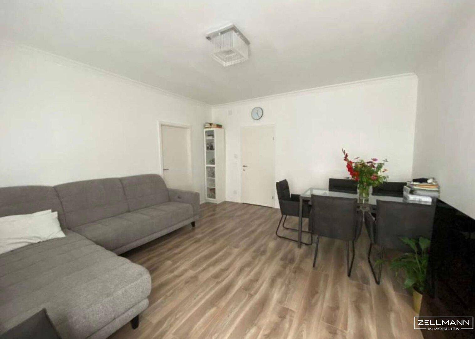 Heller Wohn- und Essbereich mit Sofa, Esstisch und Laminatboden.