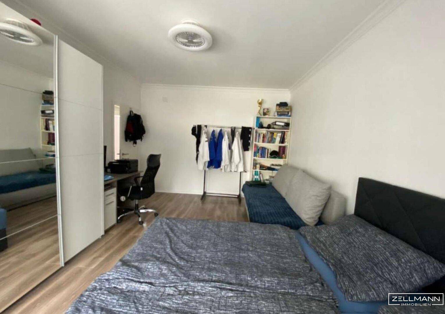 Schlafzimmer mit Doppelbett, Schreibtisch und Kleiderschrank mit Spiegeltür.