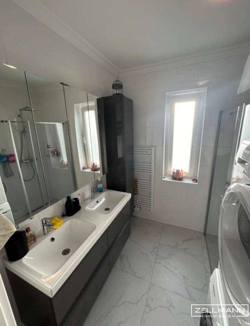Modernes Badezimmer mit Doppelwaschbecken, Spiegelschrank und Fenster.